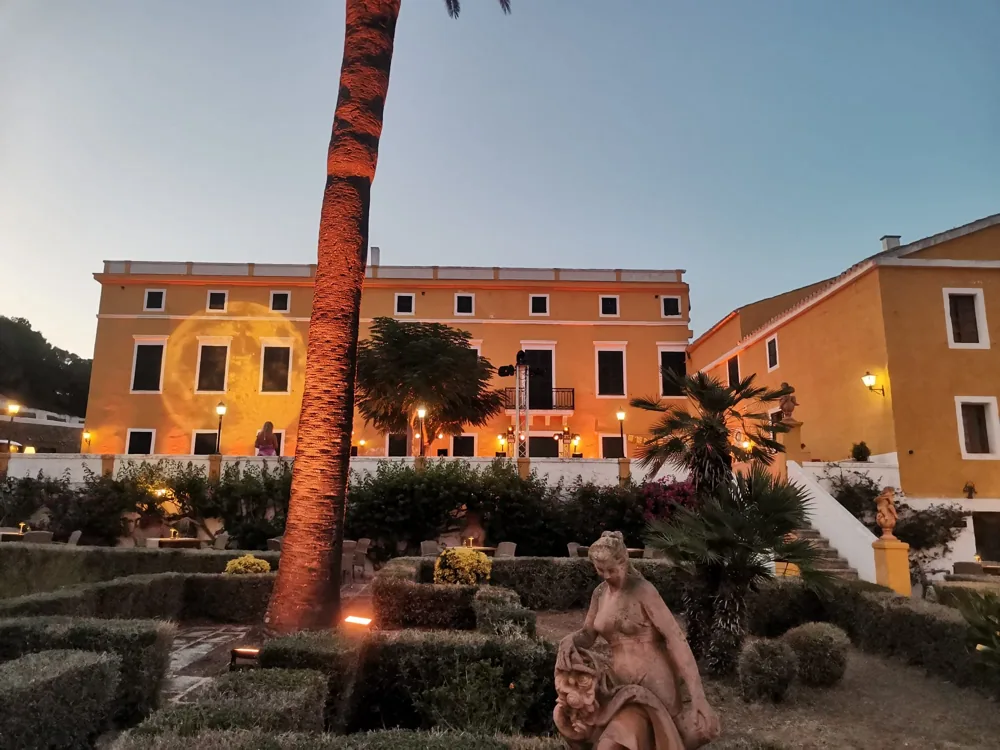 Fachada de Binissuès iluminada junto al jardín y las palmeras